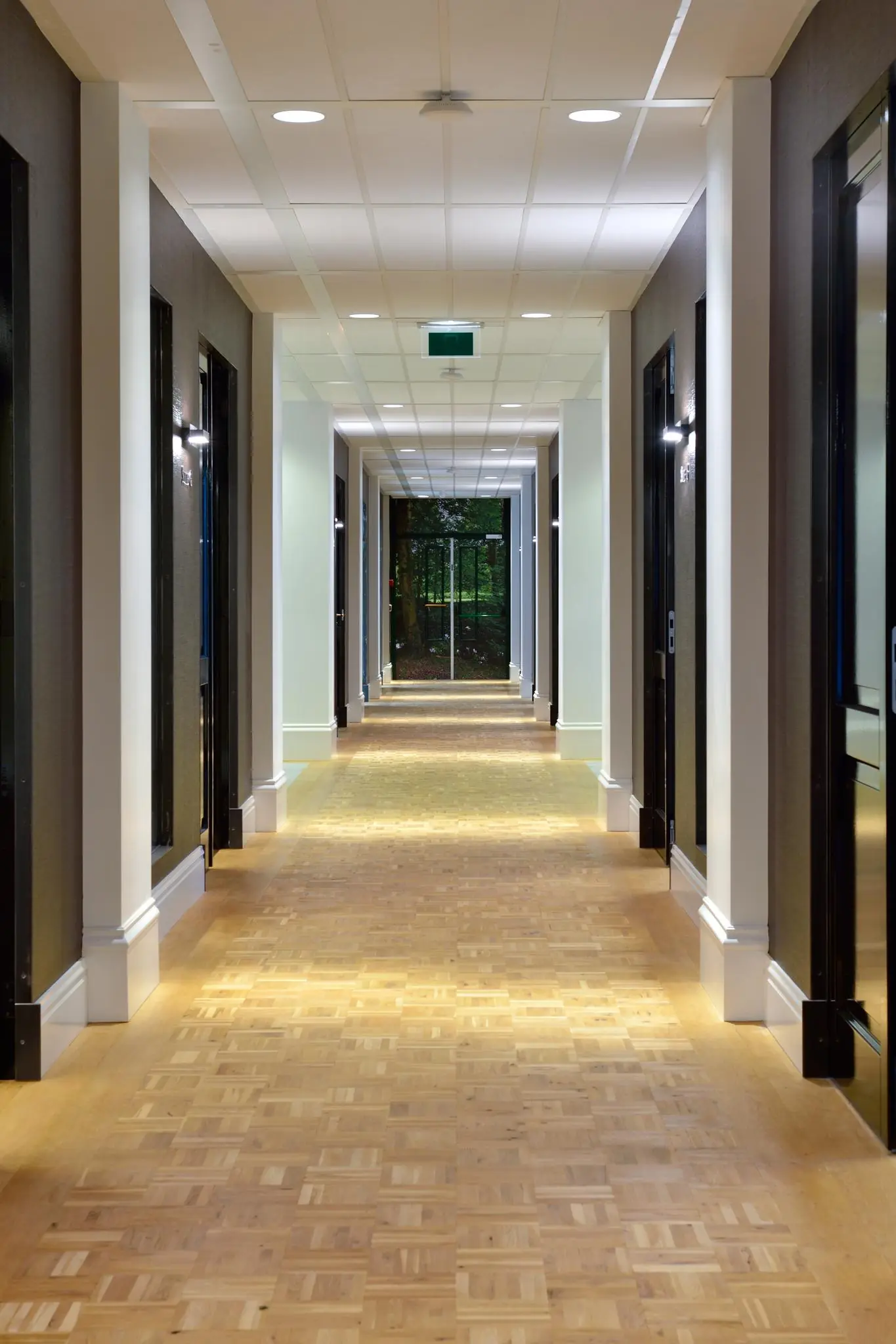 Verlichtte gang met houten vloer en zwarte deurkozijnen in een gebouw aan de Floris Grijpstraat.